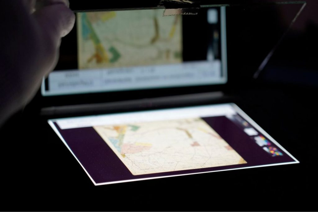 Ein großformatiges Diapositiv (Planfilm) liegt bereit zur Digitalisierung auf einem Leuchttisch und spiegelt sich in einer Glasplatte.